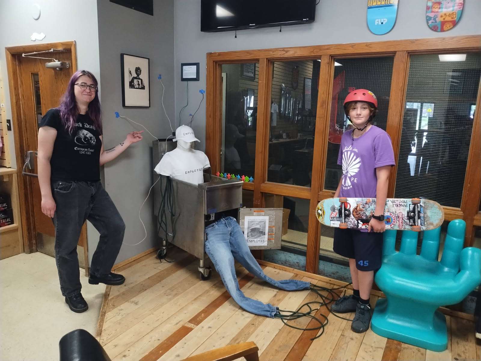 A deep fryer anchored to the wall of a skate shop using wires coming out of the back of a mannequin that has been jammed legs-first into the fryer